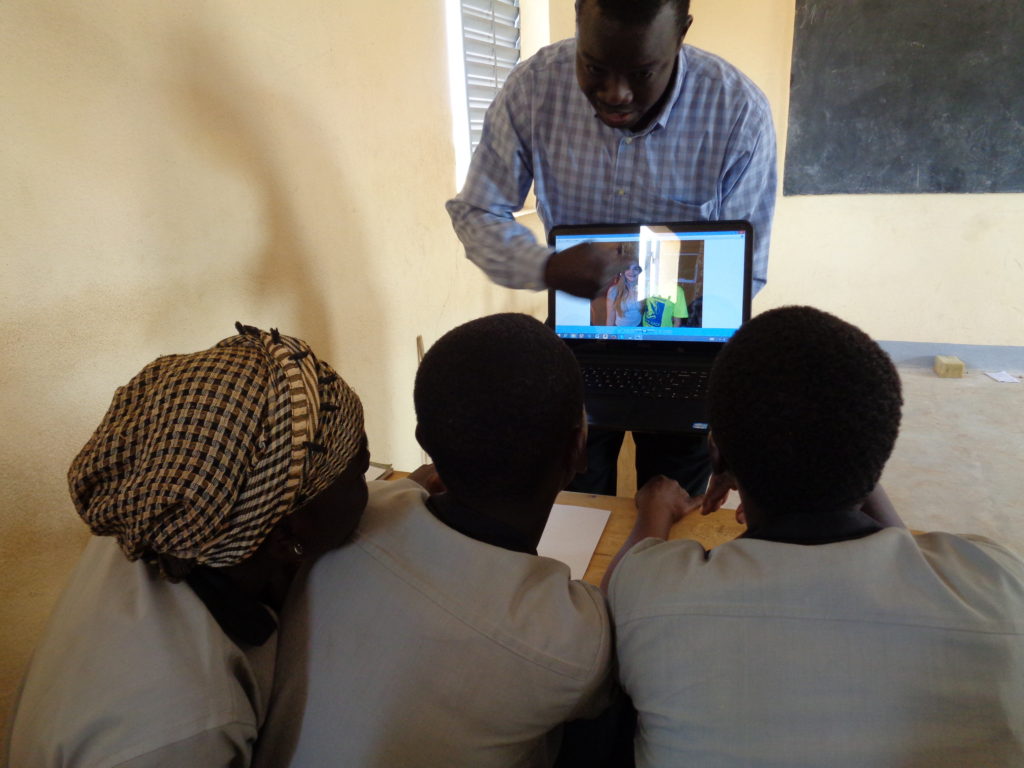 Teacher holding computer and pointing to images while students lean in