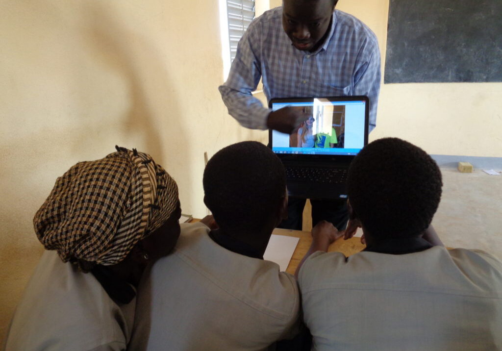 Teacher holding computer and pointing to images while students lean in